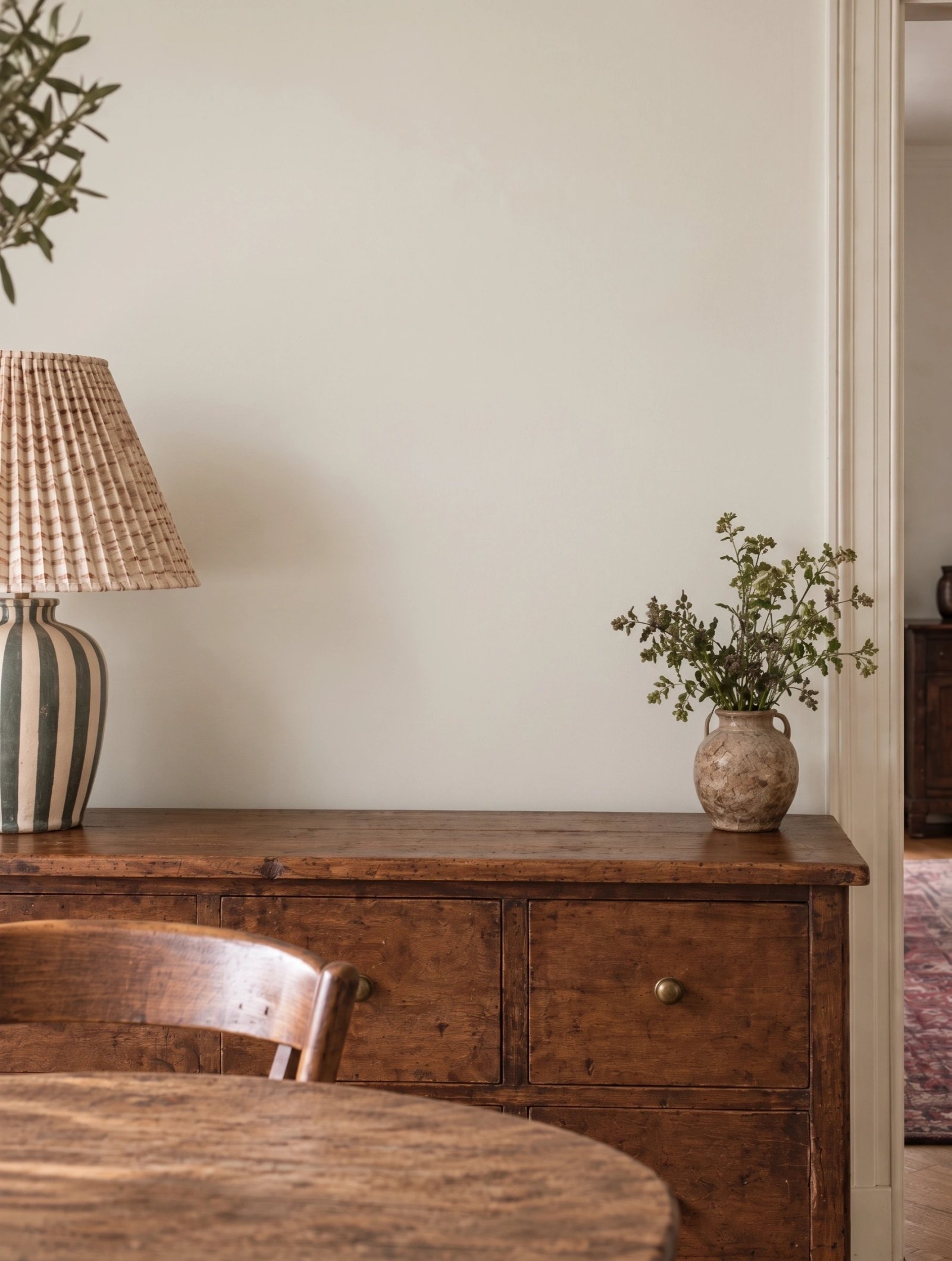 Wall art mockup: Warm contemporary dining space with antique furniture, with plants, lamps and a cabinet